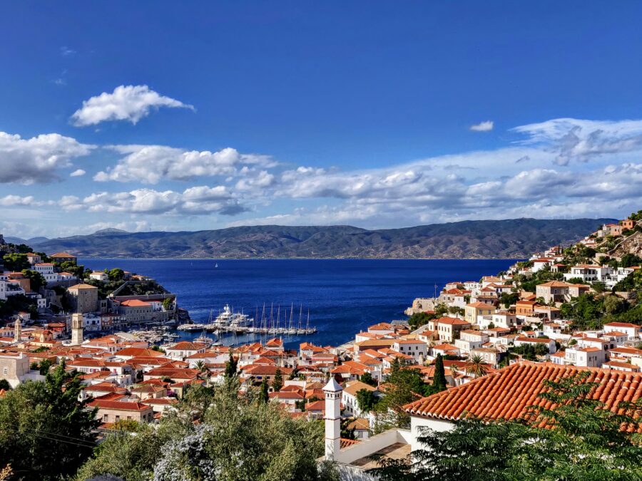 Hydra, Greece coastal town: whitewashed houses, terracotta roofs, marina, and blue Mediterranean sea.