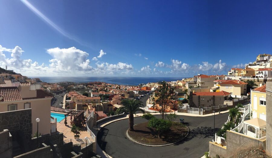 Panoramic view of vibrant Arguineguin coastal town with terracotta roofs, lush greenery, and ocean backdrop.