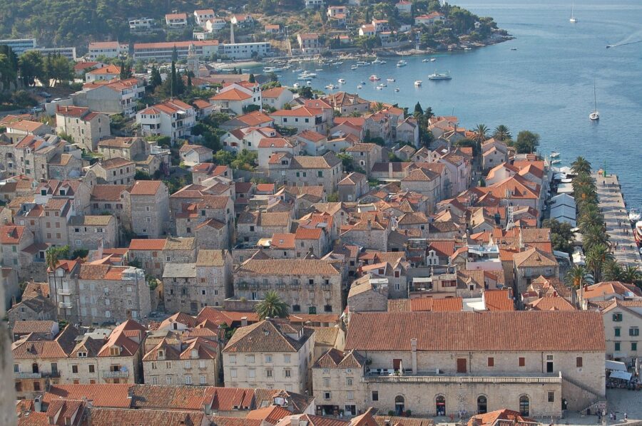 Picturesque coastal Mediterranean town with red-tiled roofs, lush greenery, and serene waterfront.