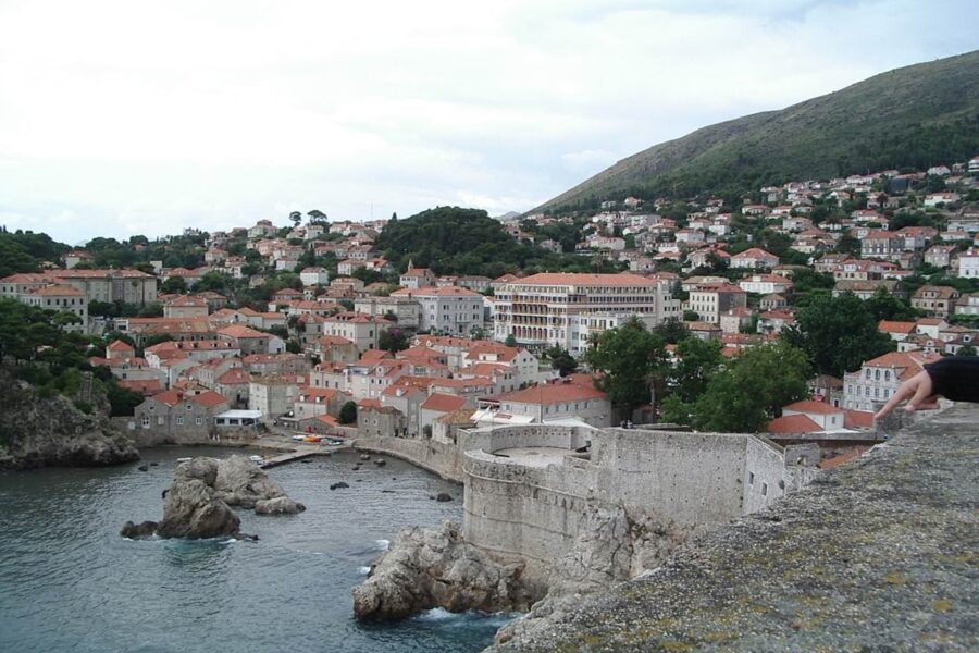 Coastal town bay with terracotta rooftops, historic stone fortress and rocky shoreline.