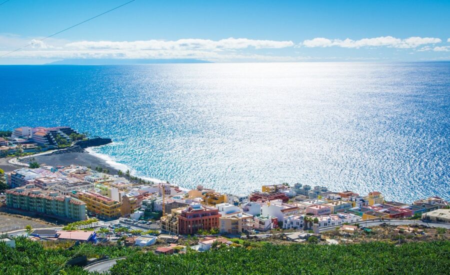 Puerto Naos coastal town and hotels overlooking turquoise ocean and rocky beach.