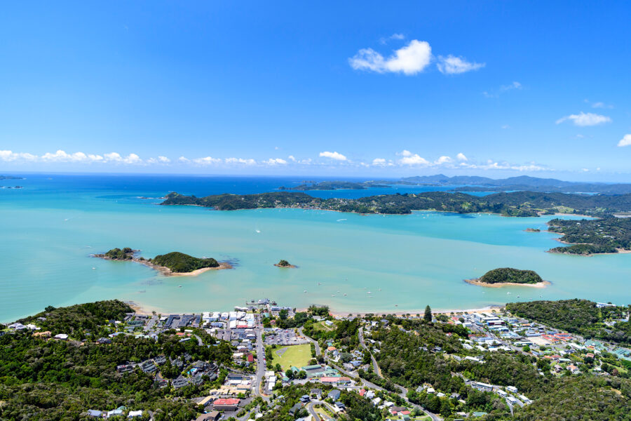 Aerial view of Paihia coastal town, turquoise bay, green islands and scenic New Zealand shoreline.