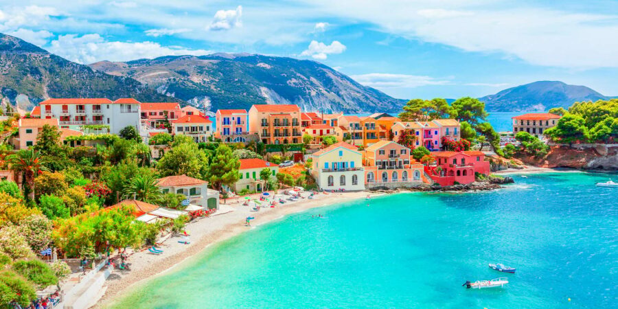 Picturesque Mediterranean beach scene with colorful buildings, turquoise waters, and mountains.