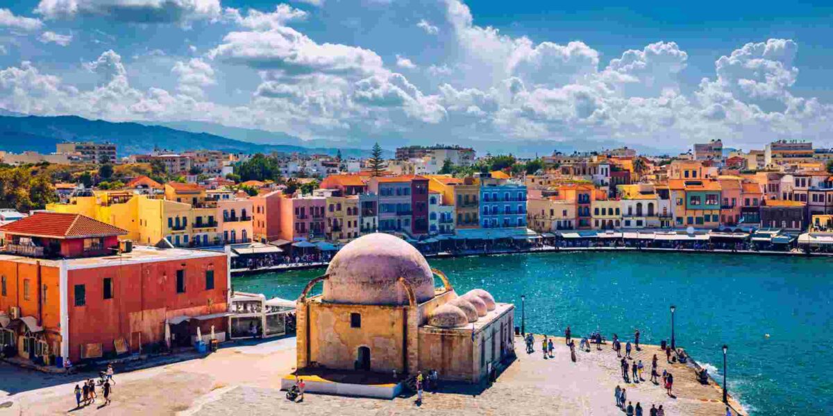 Chanias coastal scene: historic domes, colorful buildings, vibrant promenade, clear skies.