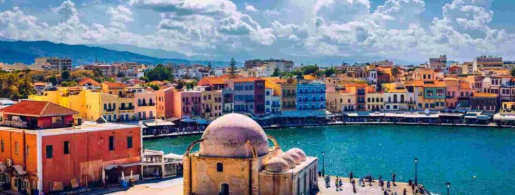 Chanias coastal scene: historic domes, colorful buildings, vibrant promenade, clear skies.