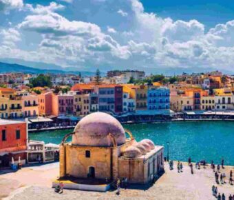 Chanias coastal scene: historic domes, colorful buildings, vibrant promenade, clear skies.