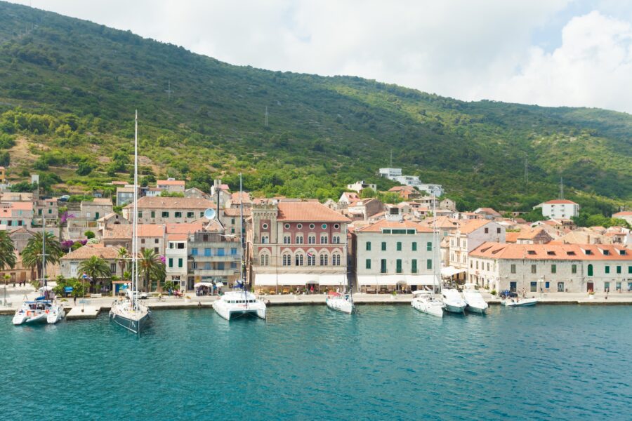 Charming coastal village harbor with boats, lush hills, and varied architecture in Komiža.