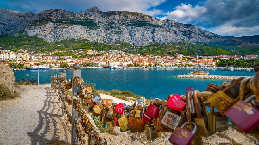 Coastal town with padlocks, Mediterranean architecture, scenic mountains, vibrant waterfront, love symbols.