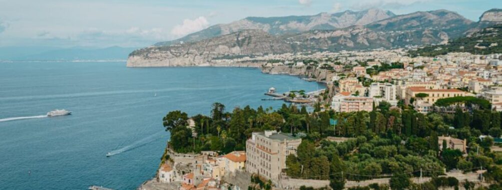 Picturesque coastal town with marina, colorful buildings, azure bay, lush greenery, hills, and sunset.