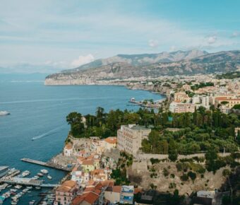 Picturesque coastal town with marina, colorful buildings, azure bay, lush greenery, hills, and sunset.
