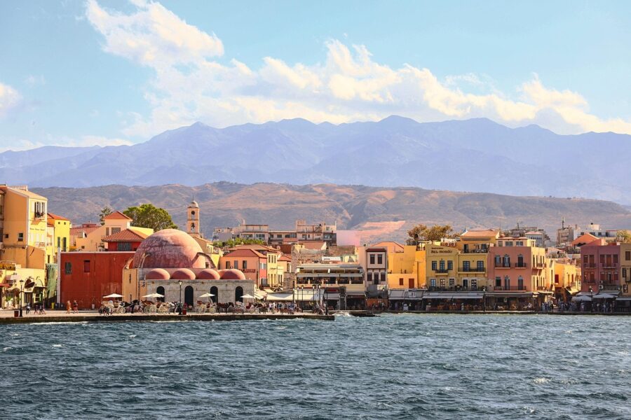 Picturesque Mediterranean harbor, colorful buildings, domed landmark, majestic mountains, tranquil waterfront.