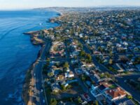 Aerial view of coastal neighborhood with ocean, boats, diverse homes, and winding roads.