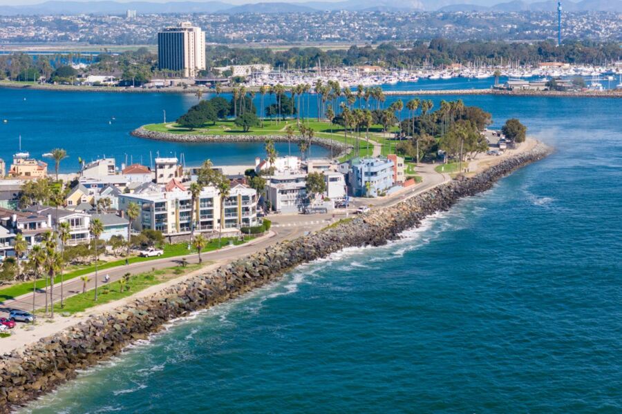 Vibrant coastal scene with boats, buildings, palm trees, lush park, and rolling hills.