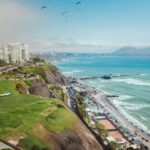 Urban Lima coastal view with city skyline, beach, mountains, and paragliders in a tropical setting.