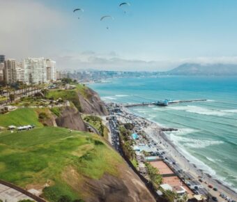 Urban Lima coastal view with city skyline, beach, mountains, and paragliders in a tropical setting.