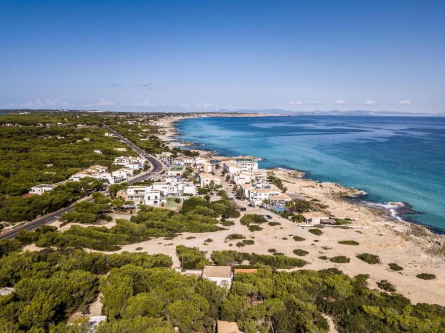 Aerial view of Es Caló coastal village with turquoise Mediterranean waters and sandy beaches.