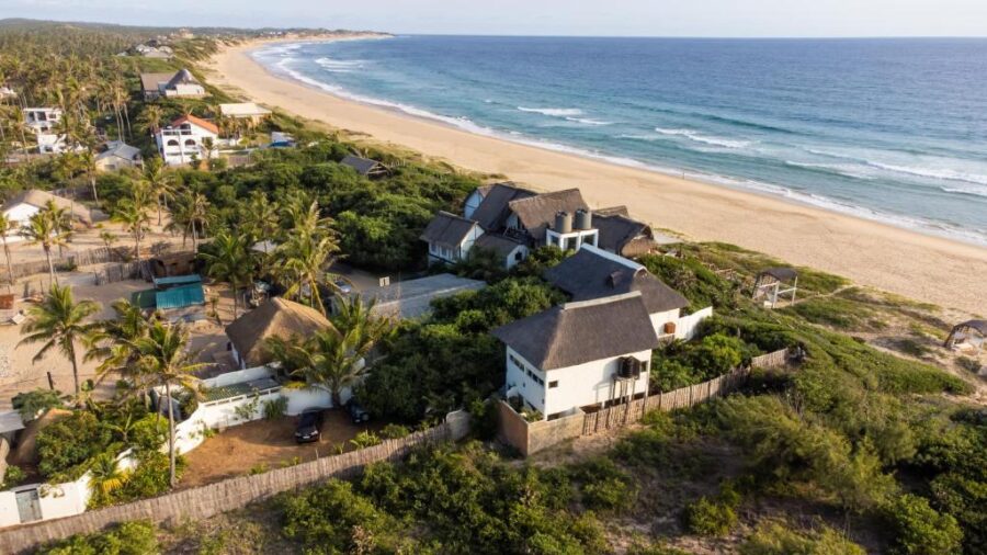 Aerial view of tropical Tofo Beach houses, secluded coastal village, golden sand shoreline, blue ocean.