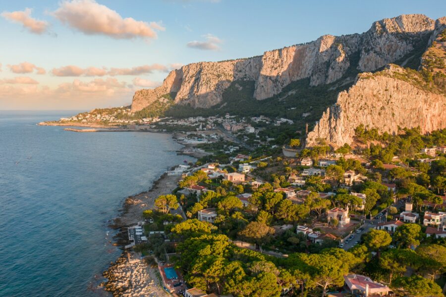Palermo, Sicily coastal village beneath towering limestone cliffs and the Mediterranean Sea.