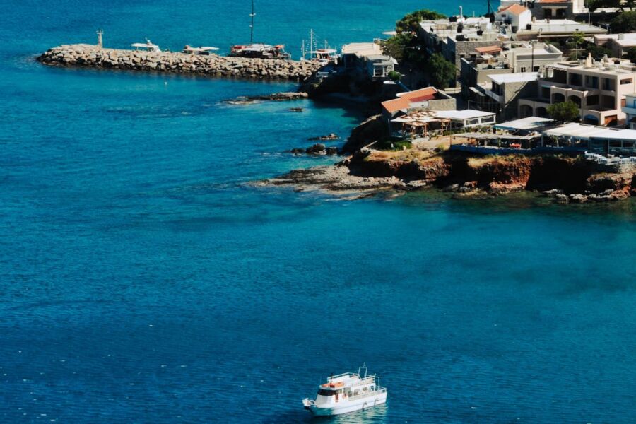 Serene coastal bay with turquoise waters, white boat, rocky shoreline, greenery, and charming settlement.
