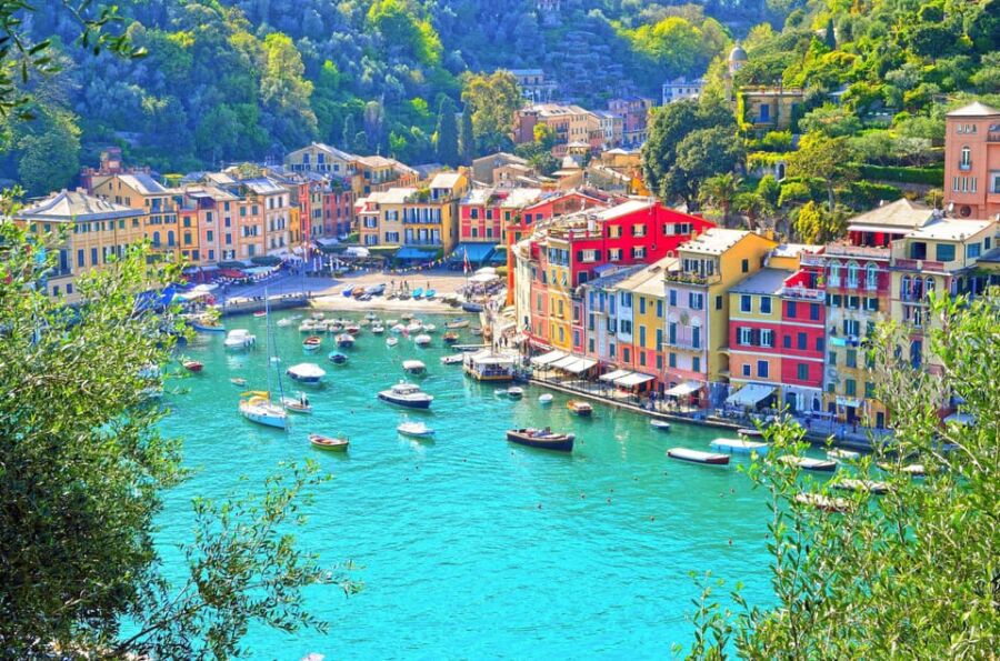 Picturesque harbor with colorful buildings, turquoise water, boats, green hills, and Mediterranean vibe.