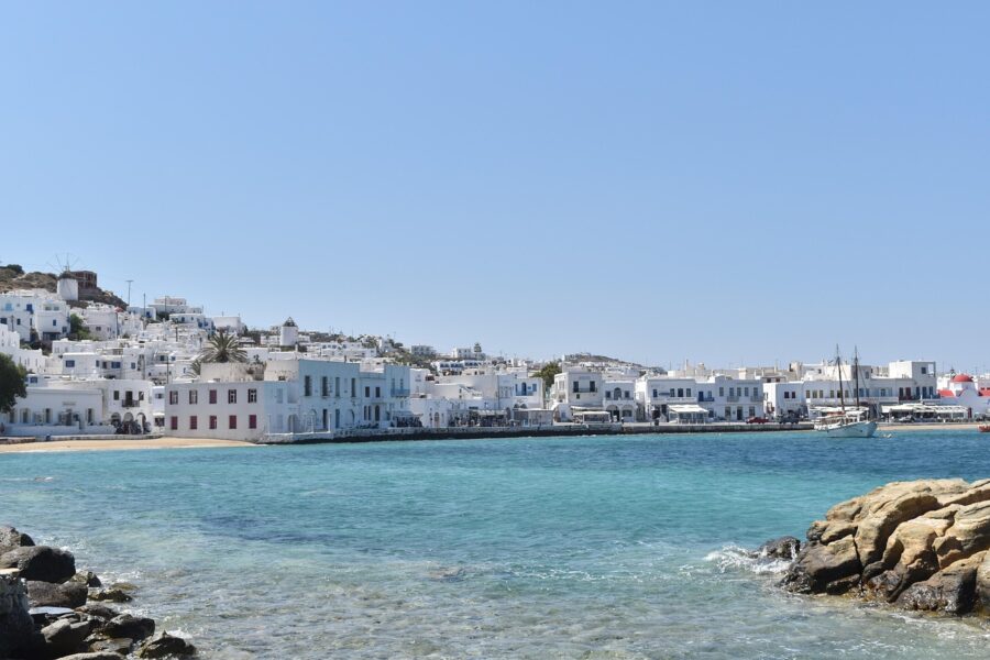 Mediterranean seaside town with whitewashed buildings, shimmering harbor, palm trees, and boats.