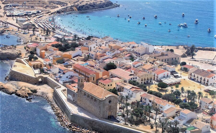 Aerial view of picturesque coastal town with beach, historic architecture, and turquoise sea.