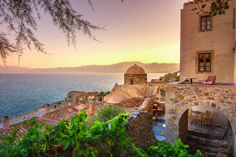 Monemvasia Mediterranean coastal village sunset with terracotta roofs, stone houses, and sea view.