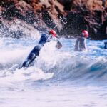 Adventure Triathlons scene with wetsuit-clad individuals against crashing waves and rugged rock formations.