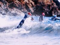 Adventure Triathlons scene with wetsuit-clad individuals against crashing waves and rugged rock formations.