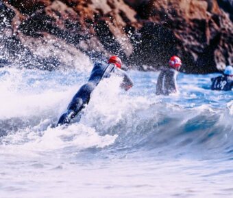 Adventure Triathlons scene with wetsuit-clad individuals against crashing waves and rugged rock formations.