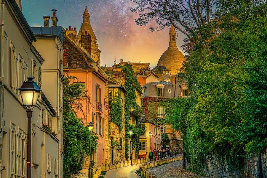 Montmartre cobblestone street at sunset with lamplight, ivy-covered houses and distant domes.