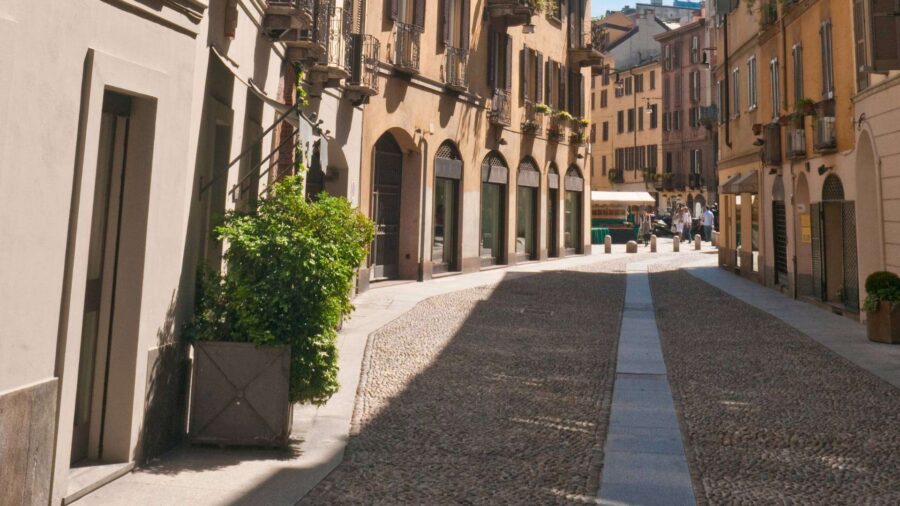 Charming historical cobblestone street with vibrant greenery, warm tones, and mingling pedestrians.