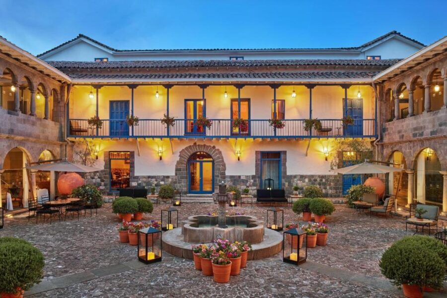 Romantic colonial courtyard hotel with stone fountain, lanterns, flowers and balconies at dusk.