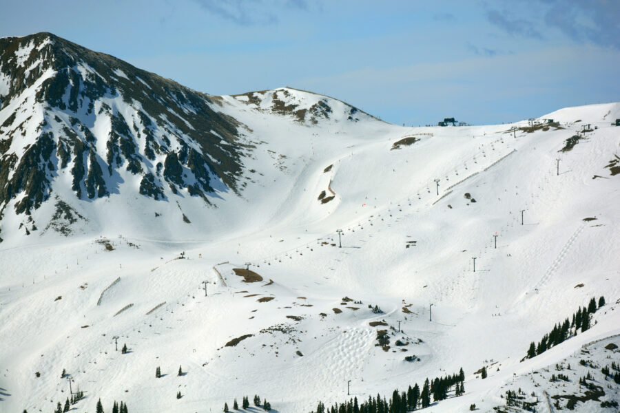 Snow-covered Arapahoe Basin Ski Area with ski slopes and pine trees under a clear blue sky