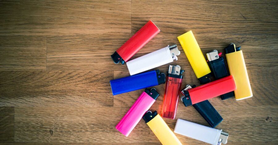 Colorful plastic lighters arranged on wood surface, various shades, casual scattered layout.