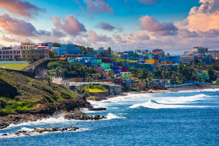 Colorful Old San Juan hillside homes overlooking rocky Caribbean coastline and ocean at sunset.