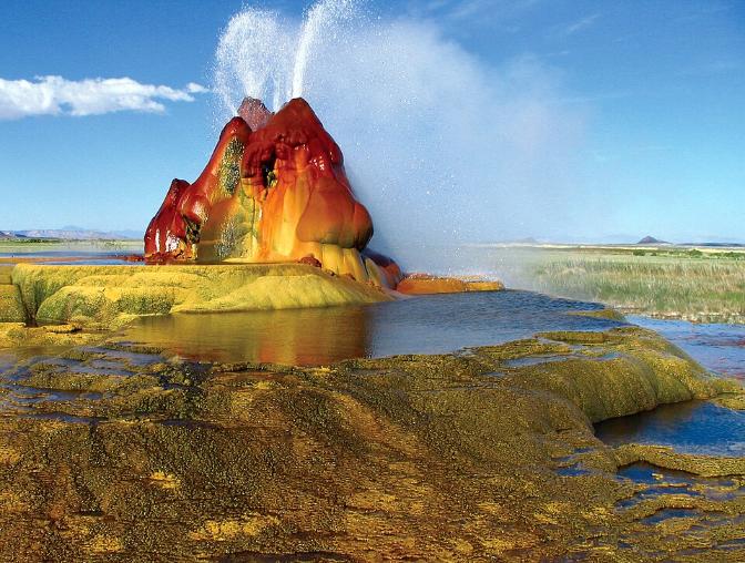 Vibrant geothermal geyser shooting steam with colorful mineral deposits and scenic landscape.