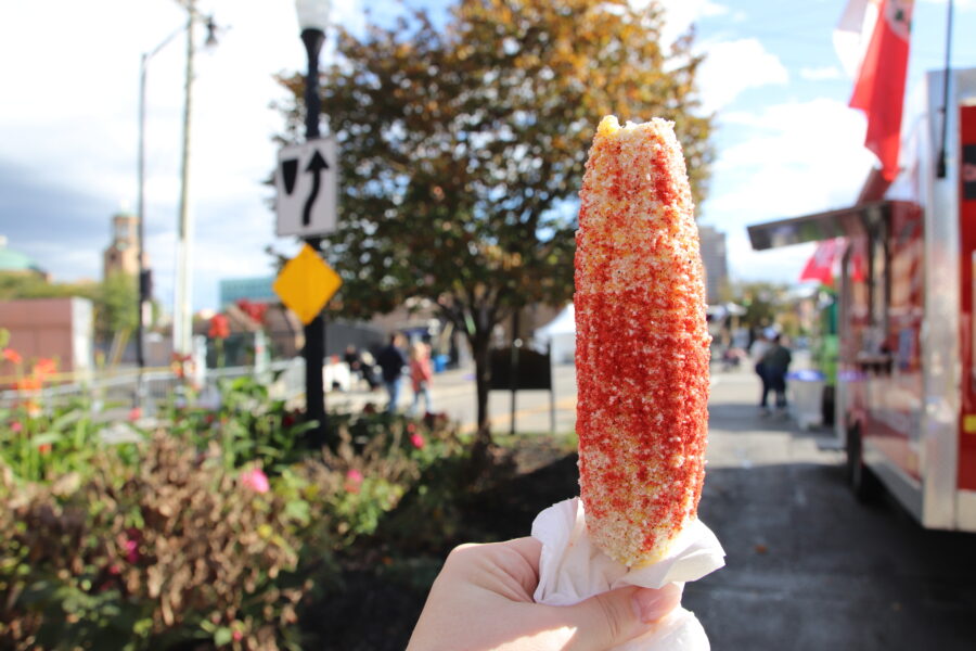 Close-up of corn on a stick, served at a lively county fair in Columbus, Ohio, surrounded by colorful fair booths.