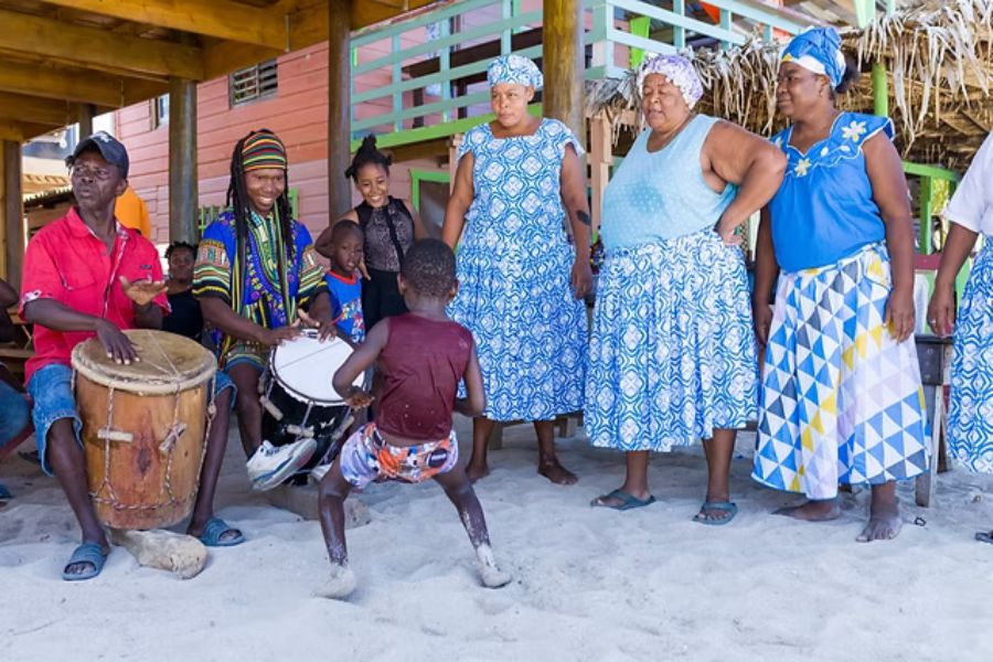 Garifuna cultural celebration with music, dance, traditional attire, and community joy on a beach.