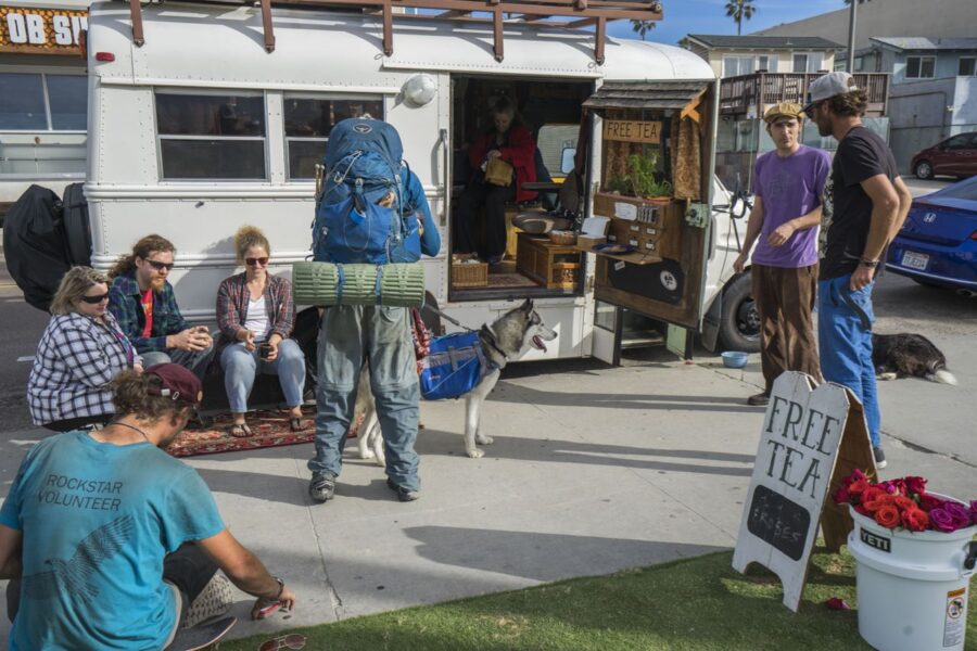 Urban gathering around repurposed bus with free tea, fostering community and adventure.