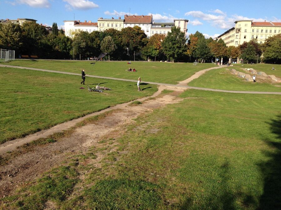 Urban park scene with autumn trees, pathway, bicycles, and people enjoying leisure activities.