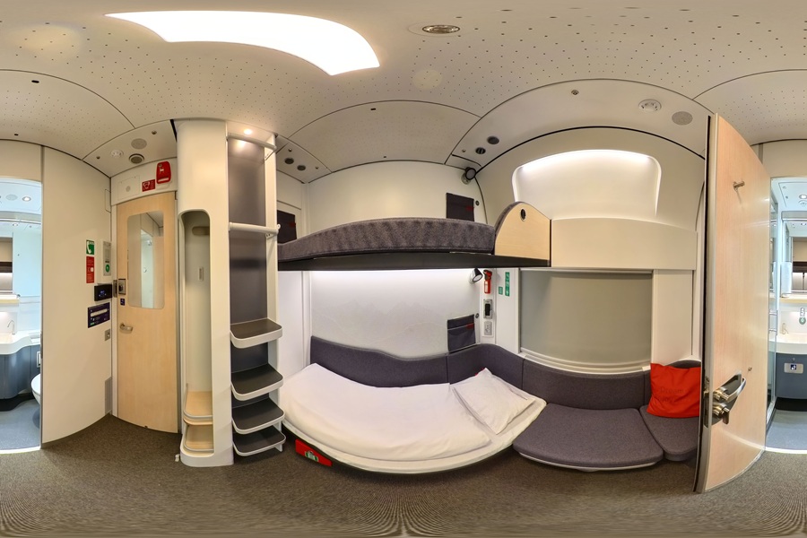 Compact train sleeper cabin with stacked bunks and built-in storage.