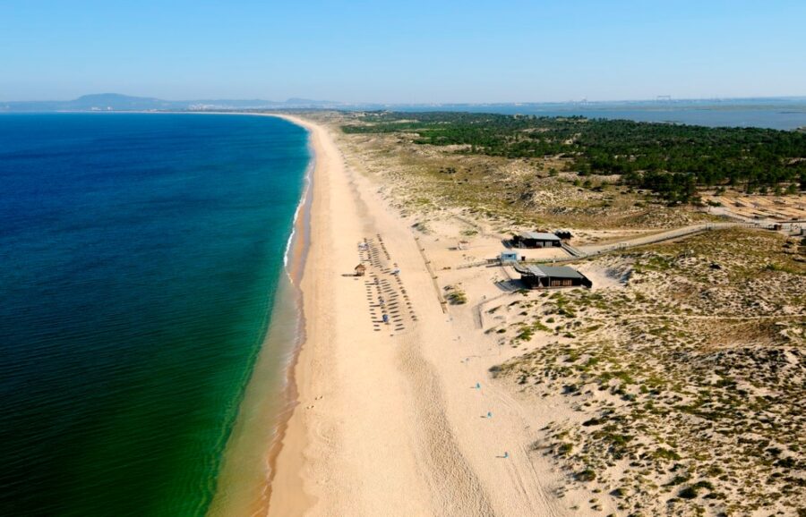Aerial view of Comporta Beach in Portugal, showcasing golden sand and a vibrant blue ocean.