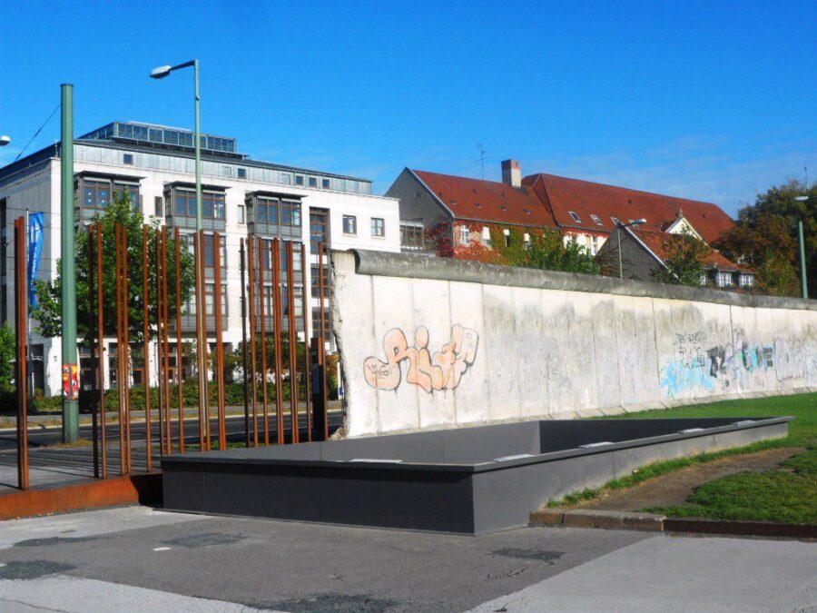 Berlin Documentation Center concrete wall with graffiti, rusted poles, modern building, red-roofed houses.