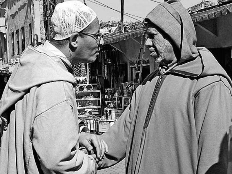 Two men in a vibrant Moroccan market exchanging a meaningful handshake.
