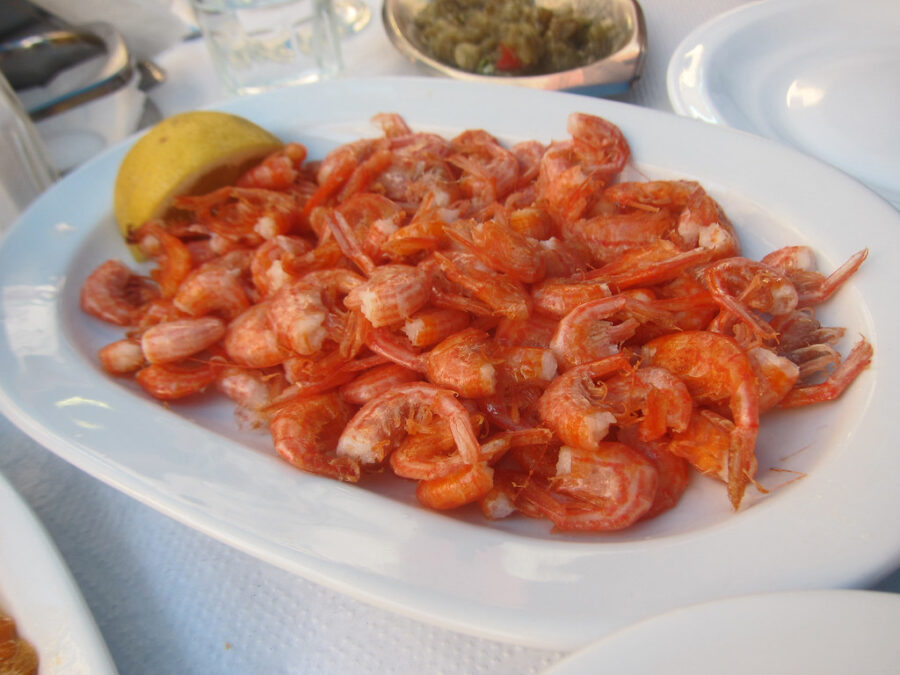 Cooked shrimp seafood platter with lemon wedge and dipping sauce.