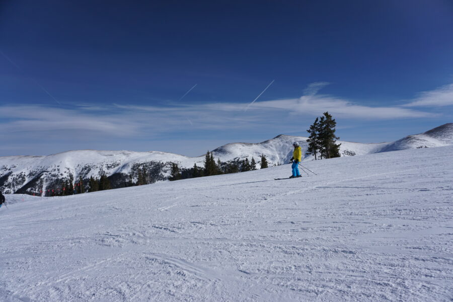 Man skiing down a snowy slope at Copper Mountain ski resort in Colorado, surrounded by pine trees and mountains.