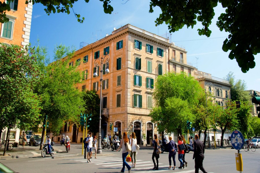 Sunlit Rome Prati corner building with shuttered windows, zebra crossing, scooters.