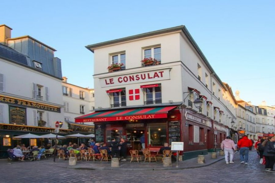 Le Consulat Parisian corner café and restaurant with outdoor terrace on cobblestone street.
