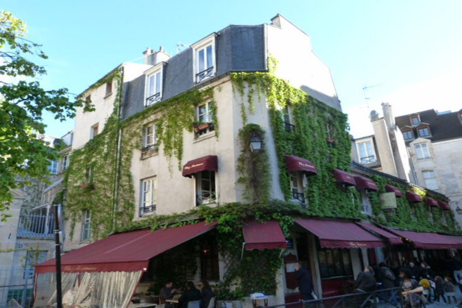 Ivy-clad Paris corner café with red awnings and outdoor terrace.